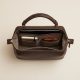 A structured leather handbag sits on a modern office desk next to a laptop.