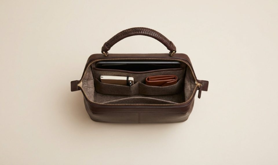 A structured leather handbag sits on a modern office desk next to a laptop.